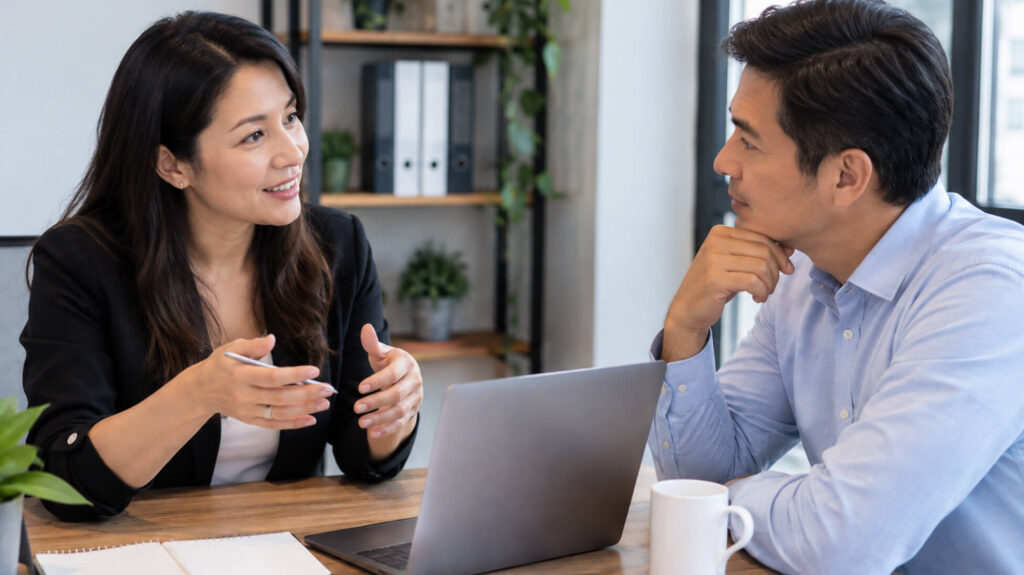 a consultant and client in genuine conversation across a desk, papers or a laptop between them — a real planning session
